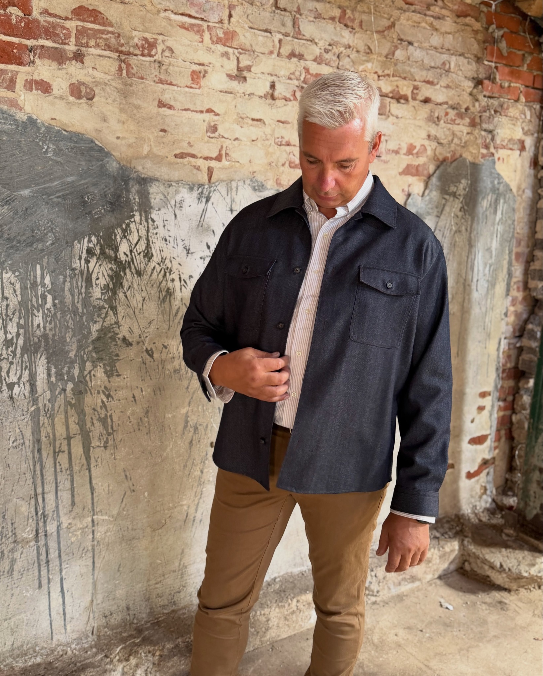 Mand i navy overshirt og camel chinos mod en patineret murvæg